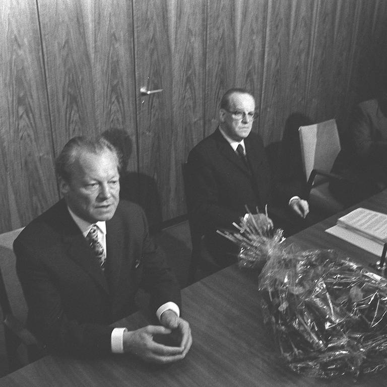 Willy Brandt (SPD, links) sitzt am 7. Mai 1974 am Tisch im Fraktionssaal, neben ihm Herbert Wehner. Auf dem Tisch ein Blumenstrauß. Am Vorabend hatte er beim Bundespräsidenten Gustav Heinemann seinen Rücktritt als Bundeskanzler eingereicht.